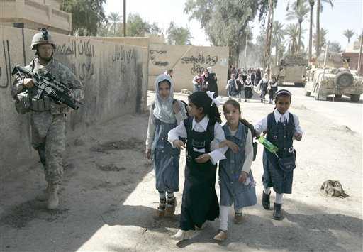 El cabo Michael Montimayer, de Chicago, Illinois, asegura el área mientras niños iraquíes caminan hacia su escuela en Salman Pak, a 45 kilómetros al sur de Bagdad. PETROS GIANNAKOURIS / AP 