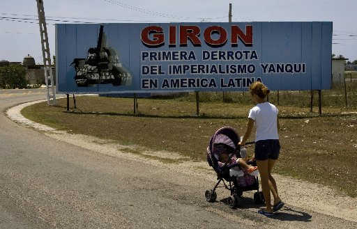 Una mujer camina a su bebé cerca de un cartel que dice: Girón, primera derrota del imperialismo yanqui en América Latina. AP 
